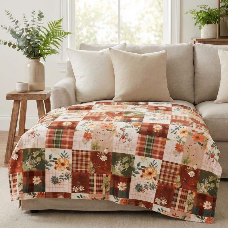 May include: A patchwork throw blanket with a mix of floral, plaid, and solid squares in shades of orange, brown, green, and cream. The blanket is draped over a beige sofa with matching pillows, creating a cozy, inviting atmosphere.