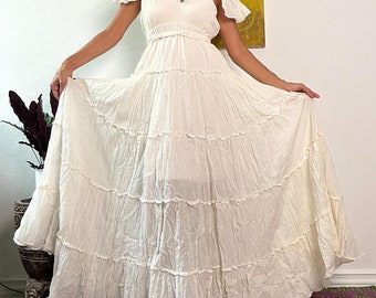 May include: A white, tiered maxi dress with a square neckline and short, ruffled sleeves. The dress is cinched at the waist with a matching sash.