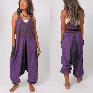 Può includere: Tuta a gamba larga e vestibilità ampia con motivo viola e nero. La tuta ha un collo a V e un laccio sulle spalle. La modella indossa la tuta con un top bianco sotto.