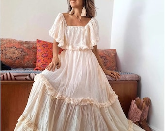 Puede incluir: Un vestido maxi blanco con escote cuadrado y volantes en capas. El vestido tiene un corte holgado y está hecho de una tela ligera.
