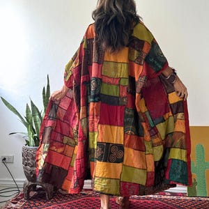May include: A long, loose-fitting kimono-style robe featuring a patchwork design of various rectangular fabric panels in shades of red, orange, yellow, olive green, and brown, with printed symbols and patterns throughout and the text JK4.
