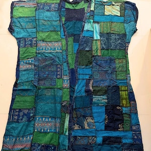 May include: A sleeveless open-front vest featuring a patchwork design composed of various blue and green fabric squares. The garment displays diverse patterns, including geometric shapes and floral motifs, with the text Style BU1 at the top.