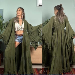 May include: A long, flowing green maxi dress with a tiered skirt and wide, ruffled sleeves. The dress has a cinched waist and a deep V-neckline.