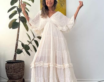 May include: A white maxi dress with a V-neckline and ruffled tiers. The dress has a flowy, bohemian style and is made of a lightweight fabric.