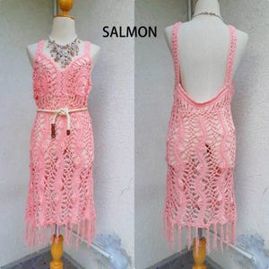 May include: A salmon pink crochet dress with a white rope belt and fringe trim. The dress has a sleeveless design and a deep V-neckline. The word "SALMON" is written in black text at the top of the image.