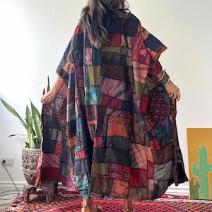 May include: A long, loose-fitting kimono-style garment featuring a patchwork design composed of various rectangular fabric panels in shades of red, blue, black, green, and brown. The garment displays diverse textures and patterns throughout.
