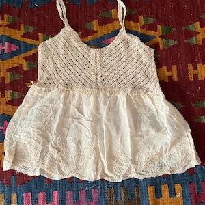 May include: Cream-coloured camisole with a crochet bodice and an embroidered skirt. The top has spaghetti straps and a V-neck. The text "Cream C" is visible. The camisole is made of soft, lightweight fabric. A vintage-style garment.