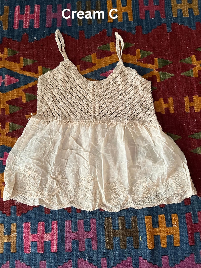 May include: Cream-coloured camisole with a crochet bodice and an embroidered skirt. The top has spaghetti straps and a V-neck. The text "Cream C" is visible. The camisole is made of soft, lightweight fabric. A vintage-style garment.