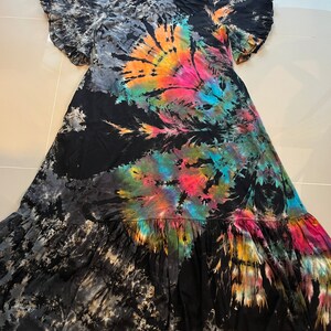 May include: A black maxi dress with a tie-dye pattern in shades of blue, pink, orange, and yellow. The dress has a ruffled neckline and short sleeves with ruffles. The dress has a tiered skirt.
