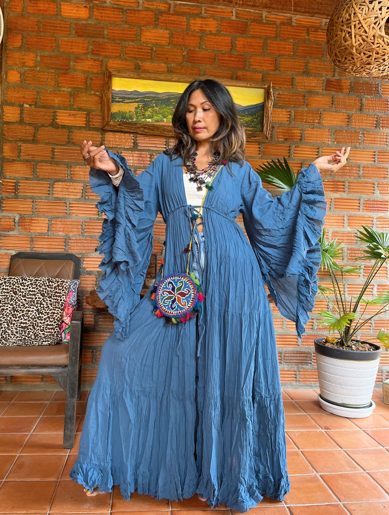 May include: A blue long-sleeved maxi dress with ruffled sleeves and a cinched waist. The dress has a tiered skirt and is made of a lightweight fabric.