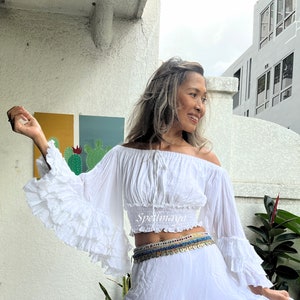 May include: White off-the-shoulder peasant top with long, ruffled sleeves and a cinched waist. The top is made of a lightweight, flowy fabric and has a relaxed fit.