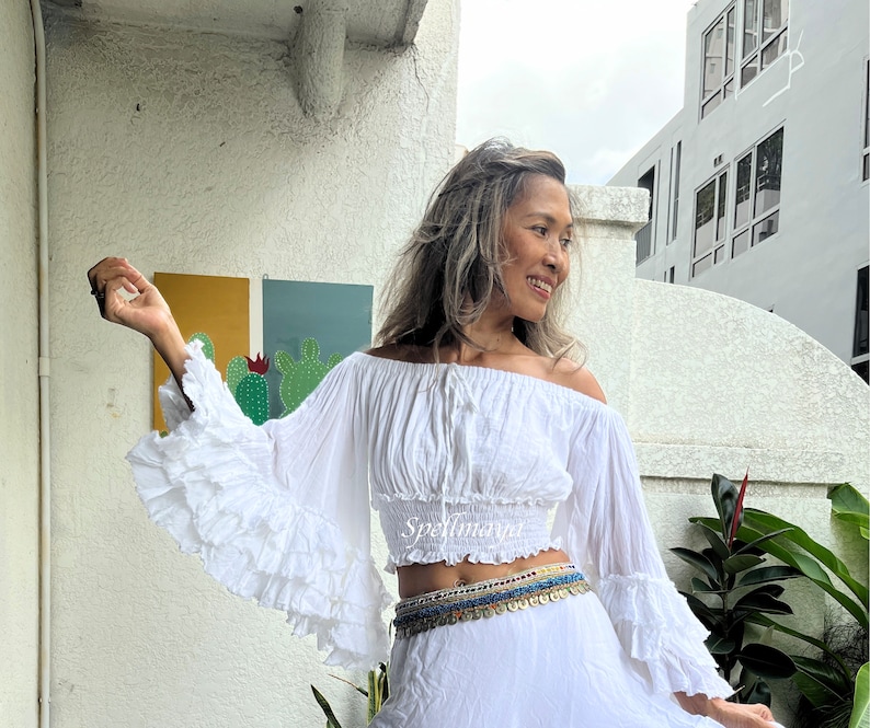 May include: White off-the-shoulder peasant top with long, ruffled sleeves and a cinched waist. The top is made of a lightweight, flowy fabric and has a relaxed fit.