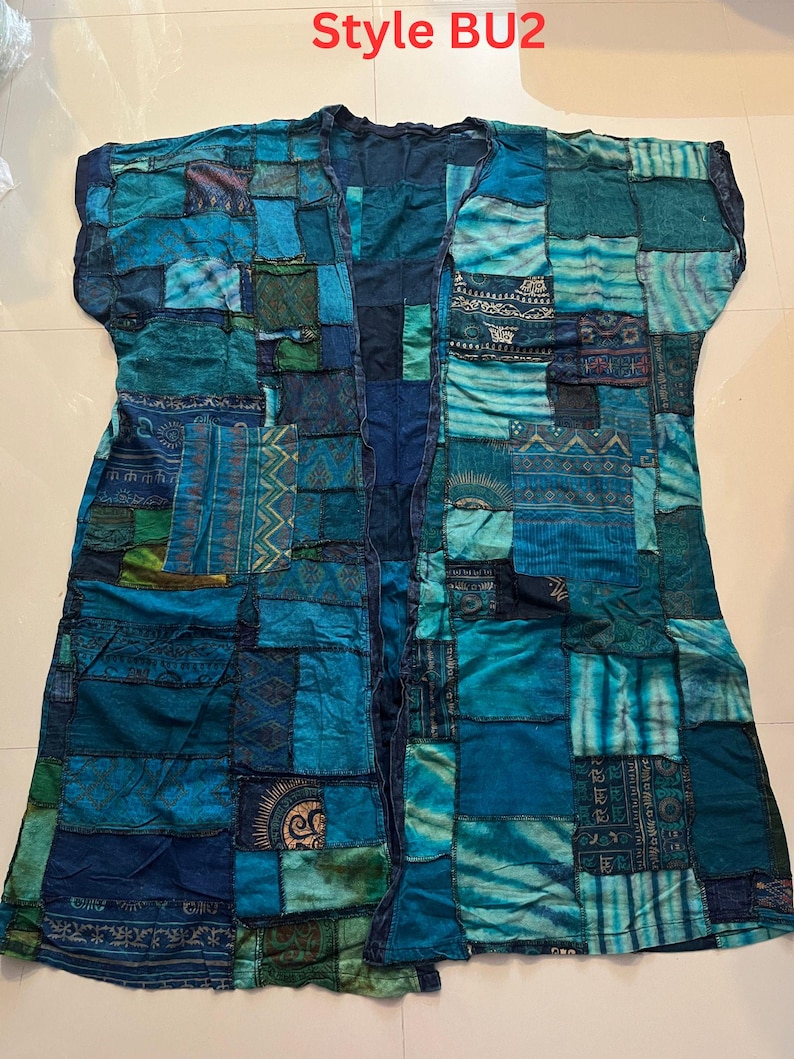 May include: A sleeveless open-front duster cardigan featuring a patchwork design in various shades of blue, teal, and green. The garment is constructed from rectangular fabric panels with diverse patterns, including geometric shapes and sun motifs. Text reads Style BU2.
