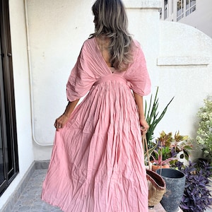 May include: A pink maxi dress with a V-neckline and a gathered skirt. The dress has a relaxed fit and is made of a lightweight fabric.