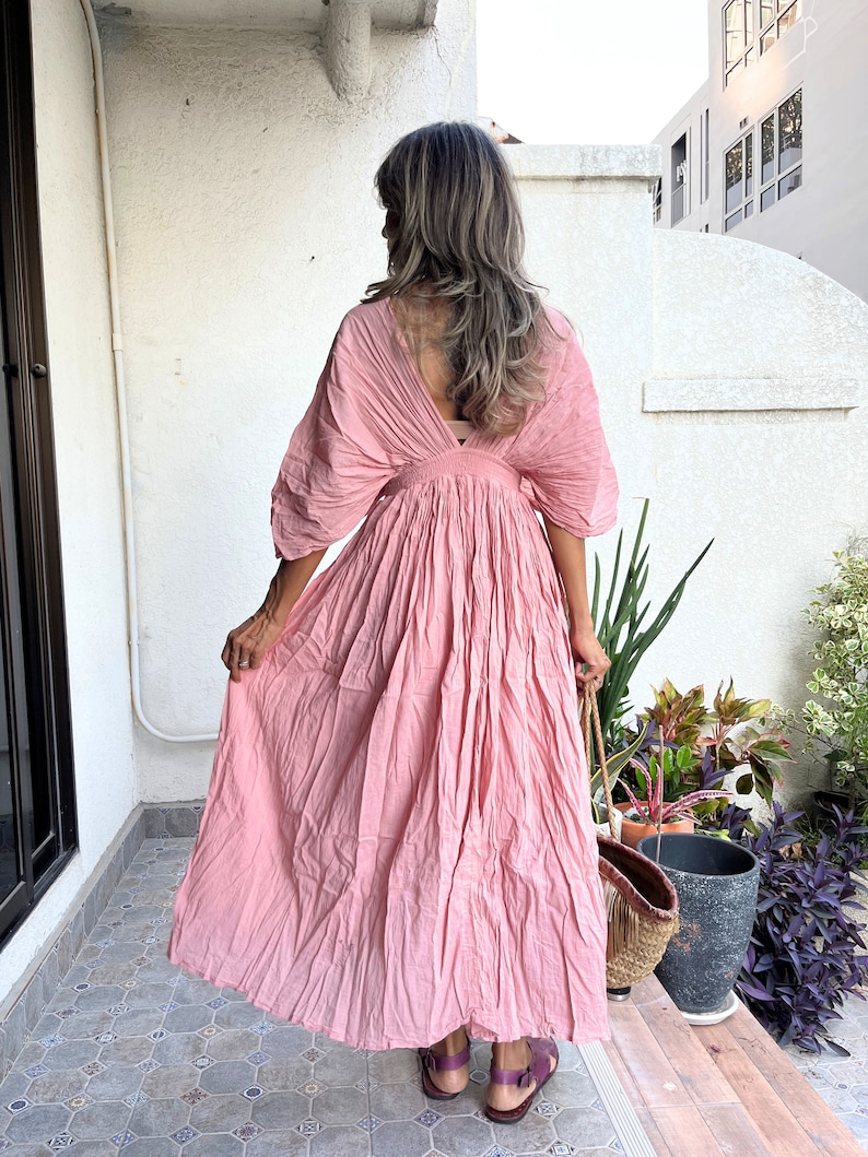 May include: A pink maxi dress with a V-neckline and a gathered skirt. The dress has a relaxed fit and is made of a lightweight fabric.
