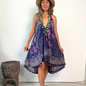 May include: A woman wearing a blue and pink floral print dress with a high-low hemline. She is wearing a brown hat and a green beaded necklace.