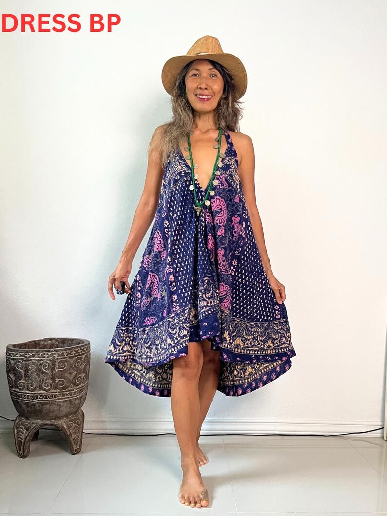 May include: A woman wearing a blue and pink floral print dress with a high-low hemline. She is wearing a brown hat and a green beaded necklace.