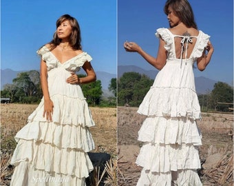 May include: A white tiered maxi dress with a ruffled neckline and a lace-up back. The dress is made of a lightweight fabric and has a flowy silhouette.