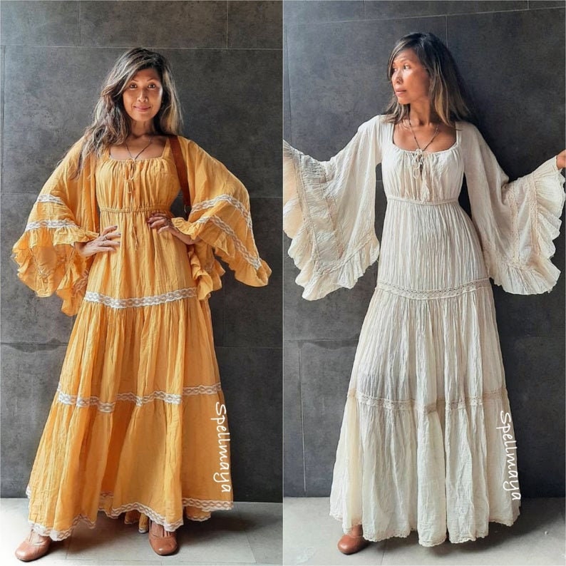 May include: Two women wearing long, flowing dresses with lace trim. The dress on the left is yellow and the dress on the right is white. Both dresses have long, bell sleeves and are tiered.