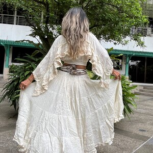 May include: A white, flowing maxi skirt with multiple layers and a ruffled hem. The skirt is made of a lightweight fabric and has a relaxed fit.