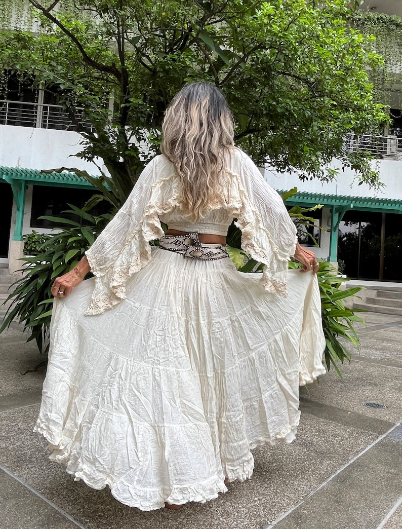 May include: A white, flowing maxi skirt with multiple layers and a ruffled hem. The skirt is made of a lightweight fabric and has a relaxed fit.