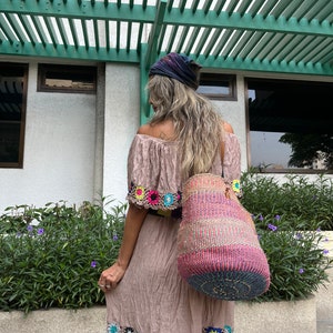 May include: A woman wearing a brown crochet dress with colorful floral accents and a large, woven, multi-colored tote bag.