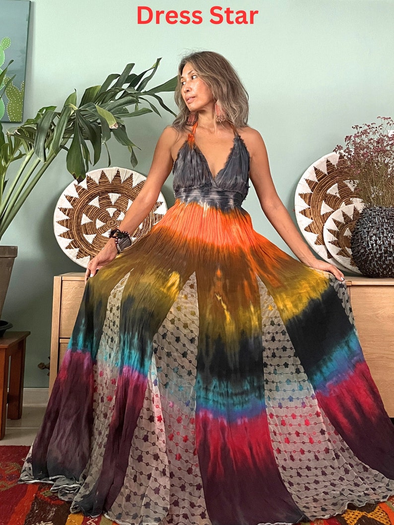 Pode incluir: Um vestido maxi longo e fluido com um padr&atilde;o tie-dye em tons de laranja, amarelo, azul e vermelho. O vestido tem um decote halter e uma saia fluida.