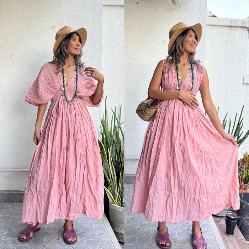 May include: Two women wearing pink maxi dresses with a gathered skirt and a V-neckline. Both women are wearing straw hats and necklaces. One woman is holding a straw bag.