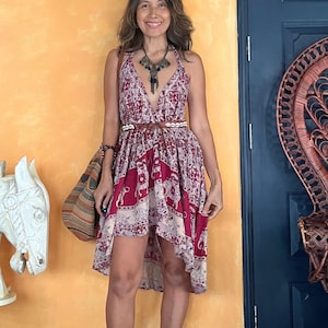 May include: A halter-neck dress with a red and cream elephant print. The dress has a high-low hemline and is cinched at the waist with a brown belt. A patterned tote bag is carried over the shoulder. The background is a yellow wall and a dark blue door.