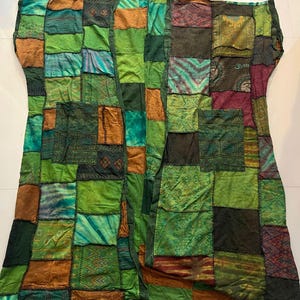May include: A patchwork kimono-style jacket featuring various shades of green, brown, and teal fabric squares with diverse patterns and textures. The garment includes two front pockets and the text Style BU5 printed at the top center.