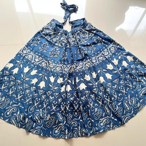 May include: A blue and white printed cotton skirt with a gathered waist and a tiered design. The skirt has a floral pattern with white flowers on a blue background.