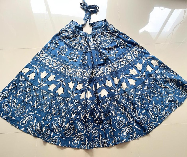 May include: A blue and white printed cotton skirt with a gathered waist and a tiered design. The skirt has a floral pattern with white flowers on a blue background.