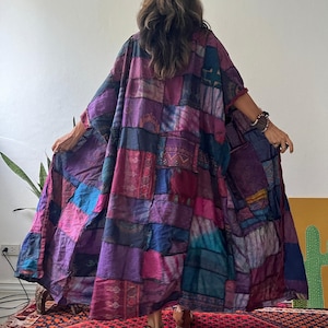 May include: A long, loose-fitting kimono-style robe featuring a patchwork design of various fabric squares in shades of purple, magenta, blue, and dark teal. The garment has wide sleeves and an open front, displaying intricate patterns on each patch.