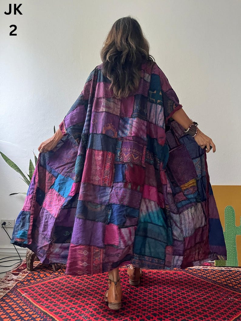 May include: A long, loose-fitting kimono-style robe featuring a patchwork design of various fabric squares in shades of purple, magenta, blue, and dark teal. The garment has wide sleeves and an open front, displaying intricate patterns on each patch.