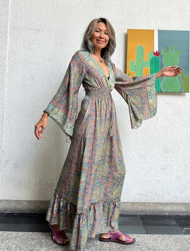 May include: A long, flowing floral print maxi dress with a V-neckline, elastic waist, and bell sleeves. The dress is a light green and pink color with a floral pattern.