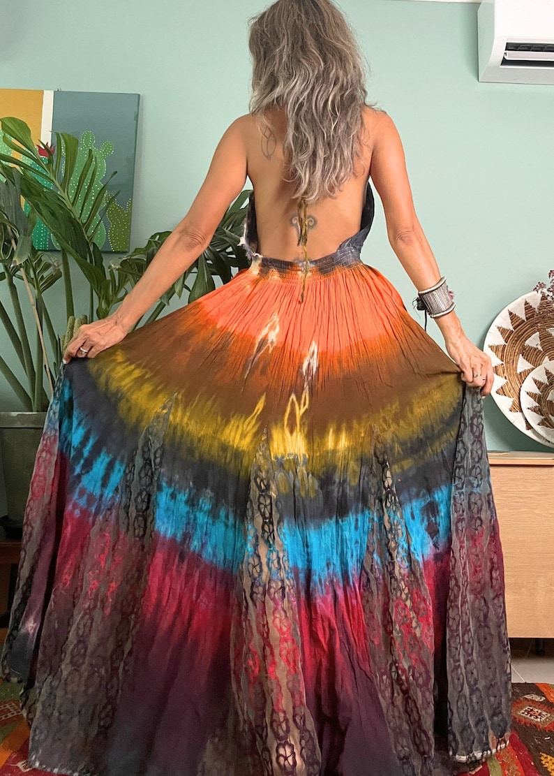 Pode incluir: Um vestido maxi longo de tie-dye com decote halter e um padr&atilde;o degrad&ecirc; colorido em tons de laranja, marrom, azul e vermelho.