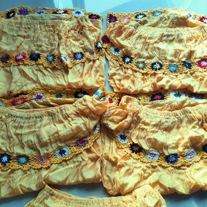 May include: Five yellow off-the-shoulder tops with crocheted trim in various colors. The tops are made of a lightweight fabric and have a ruffled design.