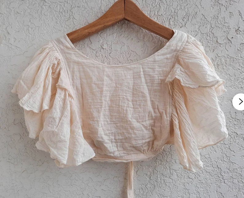 May include: A cream-colored, off-the-shoulder top with ruffled sleeves. The top is made of a lightweight fabric and has a relaxed fit.