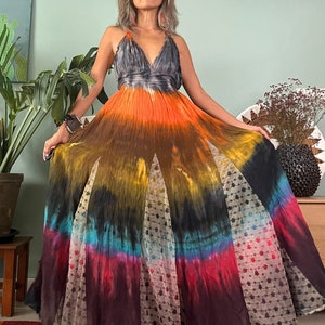 Pode incluir: Um vestido maxi tie-dye longo e fluido com decote em V e saia em camadas. O vestido &eacute; feito de um tecido macio e fluido e apresenta uma variedade de cores, incluindo laranja, amarelo, azul e vermelho.