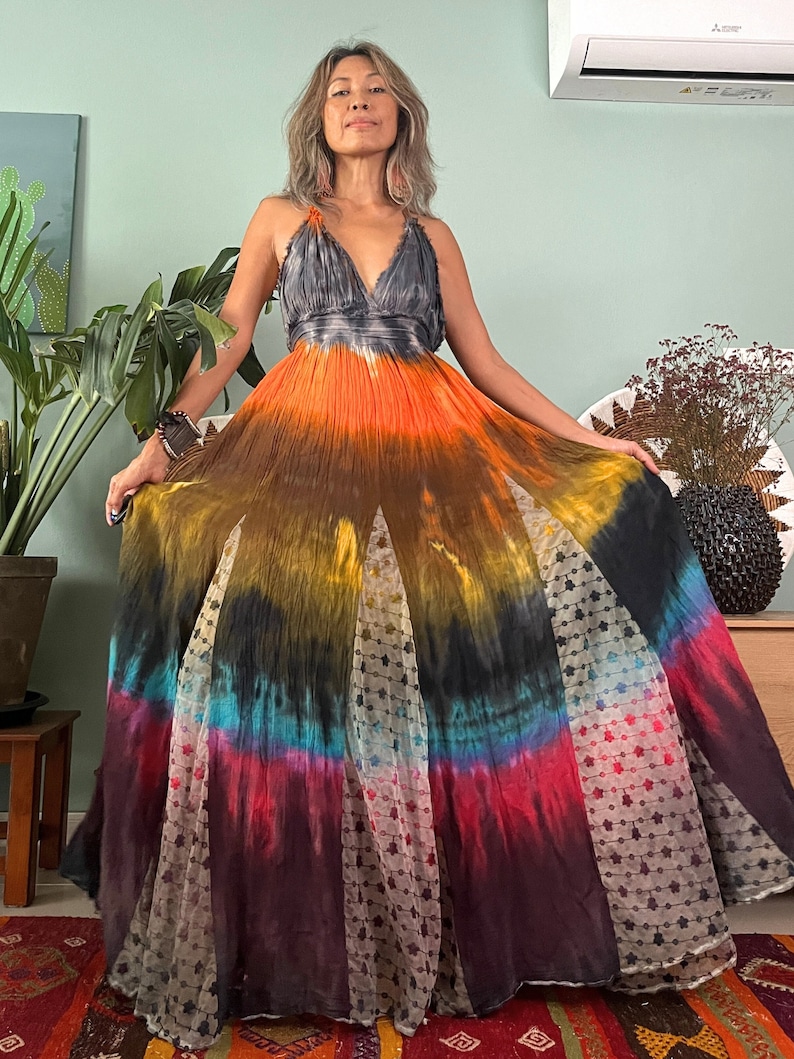 Pode incluir: Um vestido maxi tie-dye longo e fluido com decote em V e saia em camadas. O vestido &eacute; feito de um tecido macio e fluido e apresenta uma variedade de cores, incluindo laranja, amarelo, azul e vermelho.