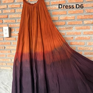 May include: A flowing, sleeveless dress with a gradient color scheme, transitioning from orange to deep purple. The dress is hanging on a black hanger against a brick wall. The text "Dress D6" is visible.