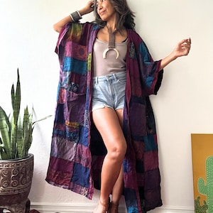 May include: A long, open-front kimono jacket featuring a patchwork design in various shades of purple, blue, and dark red. The garment has wide sleeves and a loose, flowing silhouette. The text JK 2 is visible in the upper left corner of the image.
