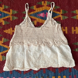 May include: Cream-coloured crochet top with spaghetti straps and a V-neck. The top has a crocheted bodice and an embroidered bottom. The text "Cream A" is visible. This is likely a summer garment, suitable for warmer weather.