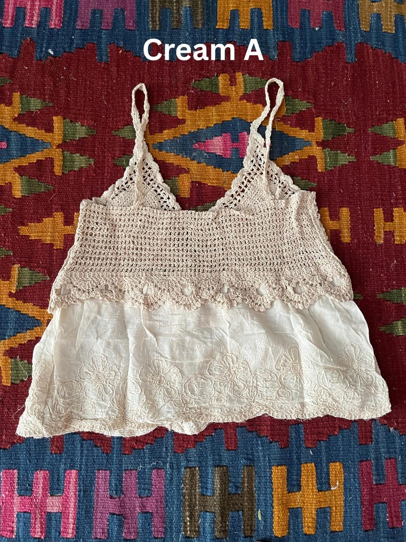 May include: Cream-coloured crochet top with spaghetti straps and a V-neck. The top has a crocheted bodice and an embroidered bottom. The text "Cream A" is visible. This is likely a summer garment, suitable for warmer weather.