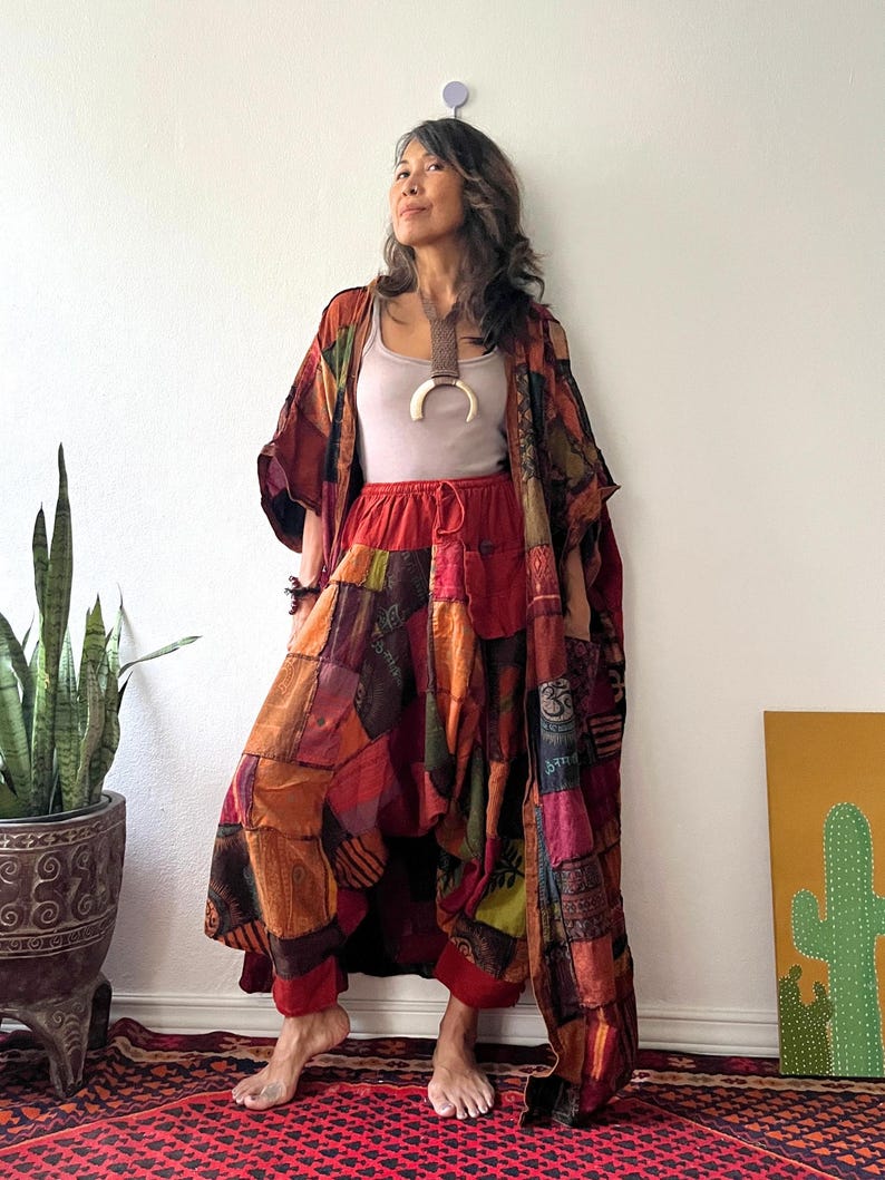 May include: A light beige tank top, a long patchwork kimono, and loose-fitting patchwork trousers. The garments feature a variety of warm-toned fabric squares in shades of red, orange, and brown, with various printed patterns and symbols throughout.