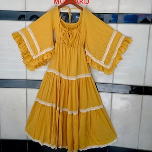 May include: A mustard yellow maxi dress with a scoop neck and bell sleeves. The dress has a lace trim and a tiered skirt.