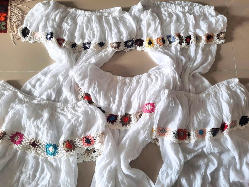 May include: Four white off-the-shoulder tops with colorful crocheted trim. The tops are made of a lightweight fabric and have a relaxed fit.