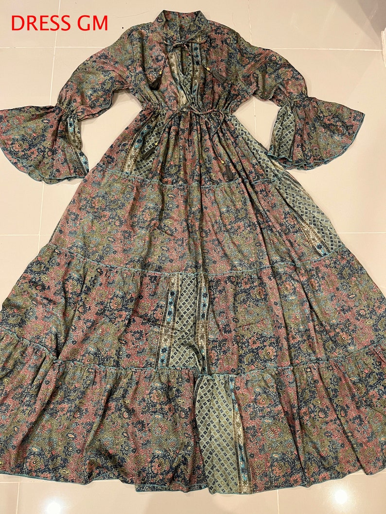 May include: A long-sleeved maxi dress with a V-neckline and a tie at the neck. The dress is made of a lightweight fabric with a paisley print in shades of blue, green, and pink. The dress has a tiered skirt and bell sleeves.