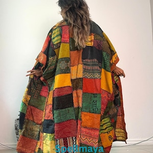 May include: A long, loose-fitting patchwork kimono-style robe featuring a vibrant array of rectangular fabric panels in shades of mustard yellow, deep red, forest green, and black. The garment displays various printed patterns and Sanskrit text.