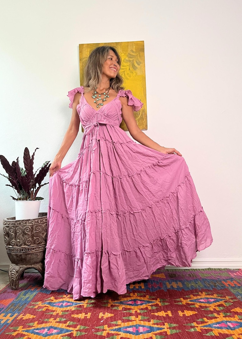 Pu&ograve; includere: Un lungo abito maxi color malva fluido con scollo a V, maniche a volant e gonna a strati. L'abito &egrave; stretto in vita con un laccio in tinta.